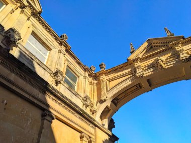 Bath, İngiltere - 30 Ocak 2025: Açık mavi gökyüzü altında tarihi Gürcistan mimarisinin ayrıntılı taş işçiliğinin ve görkemli kemerinin sergilendiği yukarı manzara