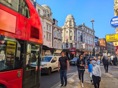 Londra, İngiltere - 10 Nisan 2025: Klasik kırmızı çift katlı otobüs, parlak mavi gökyüzü altında tarihi tiyatroların yer aldığı West End 'deki kalabalık bir Shaftesbury Bulvarı' nda yayaların yanından geçiyor