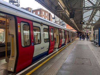 Londra, İngiltere - 26 Nisan 2025: Hammersmith ve City Line 'ın kırmızı ve beyaz bir Londra metro treni Hammersmith istasyonunda kapılar açık duruyor, yolcular tarihi çatı altında yürüyor