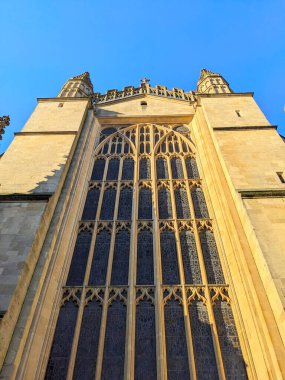 Bath, İngiltere - 30 Ocak 2025: Bath Abbey 'nin ikonik Gotik cephesi açık mavi bir gökyüzünün altında, karmaşık taş oymaları ve büyük vitray pencereleri vurguluyor.
