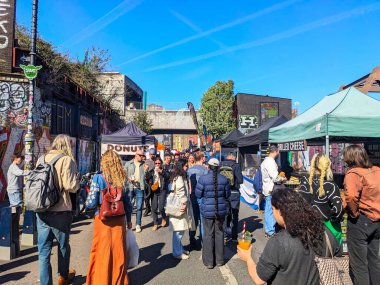 Londra, İngiltere - Nisan 06 2025: Canlı bir kalabalık, Brick Lane 'deki açık hava pazarında kentsel mimariye ve açık mavi gökyüzünün altında yiyecek ve ürün satan tezgahları keşfediyor