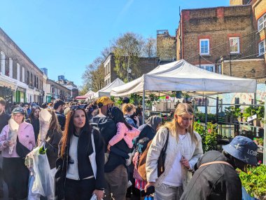 Londra, İngiltere - Nisan 06 2025: Kolombiya Yolu Çiçek Pazarı kalabalık insanların tezgahlara göz atması ve geleneksel tuğla binalar arasında güneşli bir bahar gününün keyfini çıkarmasıyla gelişiyor