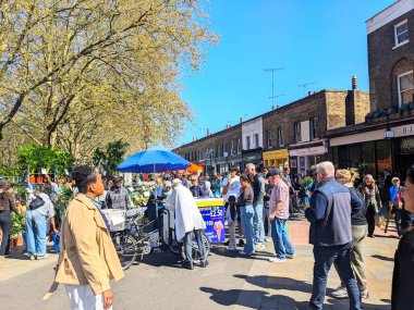 Londra, İngiltere - Nisan 06 2025: Colombia Road Çiçek Pazarı 'nda limonlu buz satan bir dondurma arabası, günışığının tadını çıkarırken, çeşitli kalabalıklarla dolu canlı bir sokak pazarı