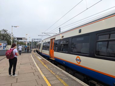 Londra, İngiltere - 02 Ağustos 2024: Willesden Junction İstasyonu platformunda günlük banliyö trafiğini tasvir eden bulutlu bir gökyüzü altında gelen Londra metro treni için bekleyenler
