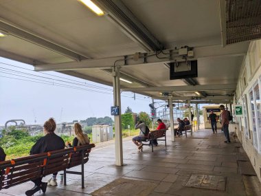 Londra, İngiltere - 02 Ağustos 2024: Çeşitli insanlar, bulutlu bir gökyüzünün altında endüstriyel bir zemini olan, yoğun Willesden Kavşak İstasyonunda Londra metro istasyonunda bekleyen bir platformda oturup bekliyorlar