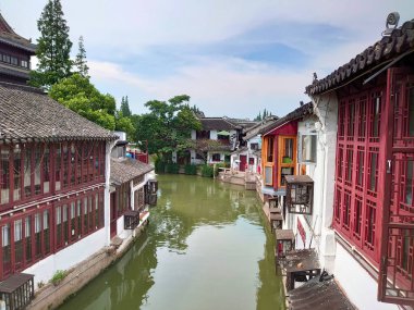 Zhujiajiao, Şangay, Çin - 25 Temmuz 2019: Geleneksel Çin mimarisi bu antik su kasabasındaki parçalı bulutlu gökyüzü altındaki tarihi binaları yansıtan sakin bir kanal su yolu çiziyor