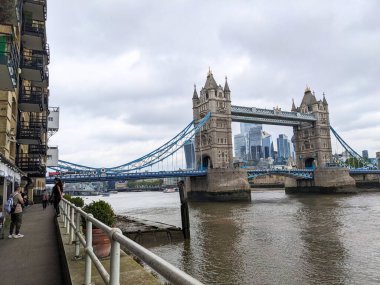 Londra, İngiltere - 13 Mayıs 2024: Tower Bridge ile fotoğraf çeken turistler ve Butlers Wharf 'taki modern Londra silueti bulutlu bir gökyüzüne karşı modern Londra siluetinin dinamik bir görüntüsünü sunuyor