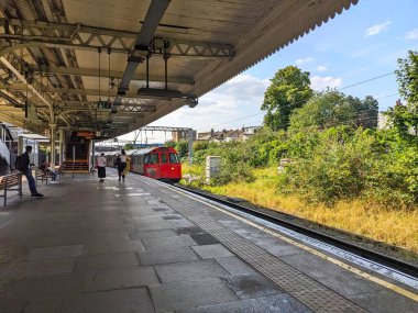Londra, İngiltere - 02 Ağustos 2024: Yolcular klasik bir kırmızı Londra Yeraltı Bakerloo Hattı treni güneşli bir gökyüzünün altında Willesden Kavşak İstasyonu 'na varırken bir platformda bekliyorlar.