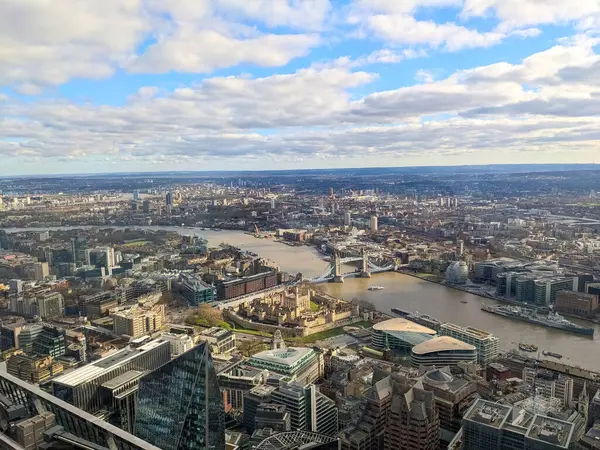 Londra, İngiltere - 16 Mart 2025: Yükseltilmiş bir panoramik manzara Thames Nehri, ikonik Tower Köprüsü ve parçalı bulutlu bir gökyüzü altında tarihi Londra Kulesi 'nin yer aldığı genişleyen Londra siluetini yakalar
