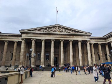 Londra, İngiltere - 27 Nisan 2023: Ziyaretçiler bulutlu bir gökyüzünün altında büyük neoklasik cephesi ve iyonik sütunlarıyla İngiliz Müzesi 'nin önünde toplandılar