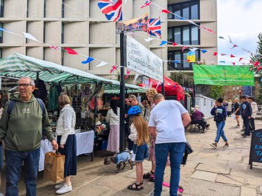 Londra, İngiltere - 30 Nisan 2023: Canlı Greenwich Vintage Marketi 'ndeki bunting ve bayraklarla süslenmiş pazar tezgahlarına göz atan kalabalık bulutlu bir gökyüzü altında canlı şehir atmosferini yakalıyor