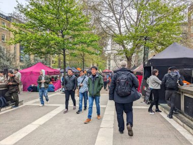 Londra, İngiltere - 27 Nisan 2023: Değişik bir grup insan Torrington Meydanı 'ndaki canlı bir açık hava pazarında geziyor ve renkli satıcılar sokak yiyecekleri ve yemyeşil ağaçlar satıyor.