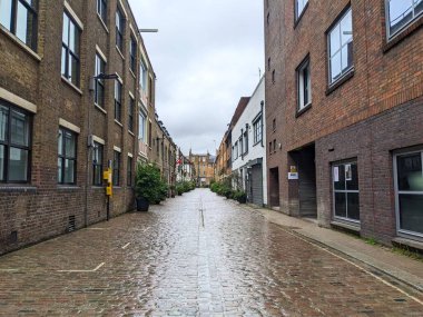 Londra, İngiltere - Mayıs 06 2023: Şehirde yağmurdan ıslanmış tarihi bir ara sokak, geleneksel tuğla binalar arasındaki bulutlu gökyüzünü yansıtarak sakin bir kent manzarası yaratıyor