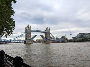 Londra, İngiltere - 11 Temmuz 2023: Tower Bridge Thames Nehri 'nde bulutlu bir gökyüzü altında bir tekne geçişine izin vermek için ikonik bazukalarını kaldırdı
