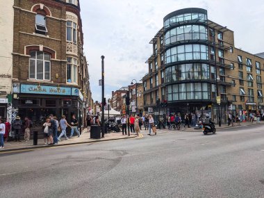 Londra, İngiltere - Temmuz 09 2023: Yayalar ve bisikletçiler, geleneksel tuğla bar ve kavisli cam mimariyi sokak satıcılarıyla sergileyerek canlı Brick Lane girişinde geziniyorlar