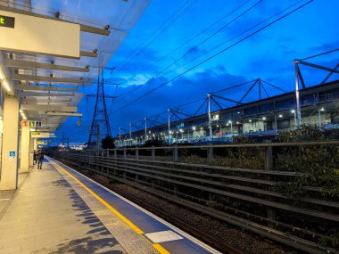 Londra, İngiltere - 01 Kasım 2023: Gümrük Evi Elizabeth Hattı istasyonunun aydınlatılmış platformu Londra Excel 'in yanında çarpıcı bir mavi saat gökyüzü altında çıkışa doğru yürüyen yolcularla birlikte parlıyor