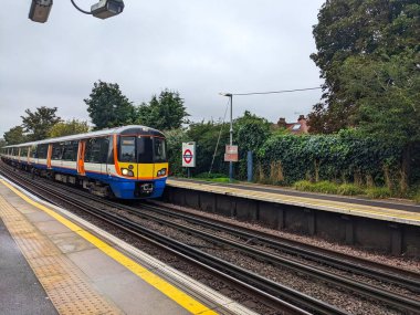 Londra, İngiltere - 12 Ekim 2023: Modern bir Londra Overground treni bulutlu bir gökyüzü altında Kew Gardens istasyonundaki boş platforma yaklaşıyor