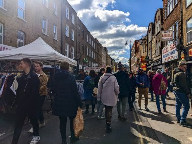 Londra, İngiltere - 3 Nisan 2022: Değişik bir kalabalık, şehrin eklektik doğu ucunda güneşli bir günde ikonik Beigel Pastanesi 'nin önünden geçen canlı Brick Lane Pazarı' nı keşfediyor
