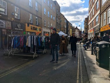 Londra, İngiltere - Nisan 03 2022: İnsanlar hareketli ve hareketli bir günde, popüler bir ziyaretçi merkezi olan Brick Lane 'de, hareketli bir sokak pazarında, ikinci el giysi için yürürler ve tararlar.