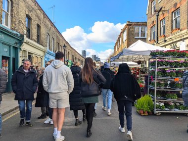 Londra, İngiltere - Nisan 03 2022: Doğu Londra 'daki canlı Kolombiya Yolu Çiçek Pazarı boyunca yürüyen büyük bir kalabalık, açık mavi bir gökyüzü altında renkli çiçeklerle göz gezdiriyorlar.