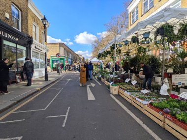 Londra, İngiltere - 3 Nisan 2022: Açık mavi gökyüzü altındaki Columbia Road Çiçek Pazarı 'nda canlı bir müşteri kalabalığı dolup taşıyor.