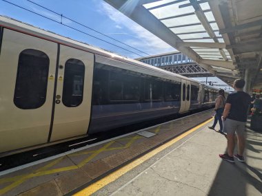 Londra, İngiltere - 16 Temmuz 2022: Gündüz Elizabeth Line treni açık bir yaz günü kalkmadan önce Slough istasyonunda dururken insanlar güneşli bir platformda bekliyorlar