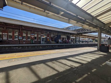 Londra, İngiltere - 16 Temmuz 2022: Yolcular klasik Viktorya dönemi mimarisine sahip Great Western Main Line 'ın önemli bir banliyö merkezi olan tarihi Slough tren istasyonunda güneşli bir platformda bekliyorlar