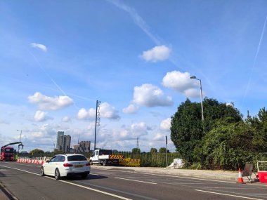 Londra, İngiltere - 21 Eylül 2021: Beyaz bir araba ve ticari kamyonlar modern binalar ve inşaat bariyerleriyle dolu, açık mavi gökyüzü altında çok şeritli Forest Yolu 'nda ilerliyorlar