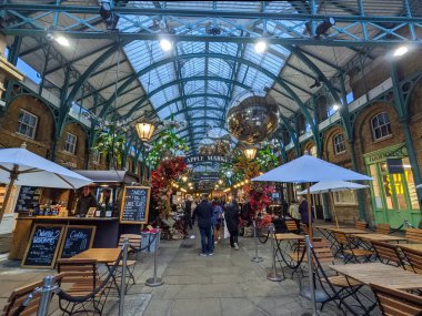 Londra, İngiltere - Kasım 05 2021: Alışverişçiler Covent Garden 'daki tarihi Apple Market' te yürüyor, ünlü Viktorya dönemi ütü ve cam çatısı altındaki şenlikli ışıklar ve dekorasyonlarla aydınlatılıyor.