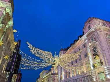 Londra, İngiltere - 21 Aralık 2021: Ünlü bir Noel ışıkları sergisinin bir parçası olan ikonik aydınlanmış bir melek, Regent Caddesi 'nin tarihi mimarisinin üzerinde parlak bir şekilde parlıyor.