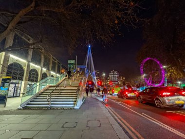 Londra, İngiltere - 21 Aralık 2021: Altın Jübile Köprüsü 'ne doğru yürüyen yayalar ve ikonik Londra Gözü ile akşam trafiği bir kış gecesinde arka planda parladı