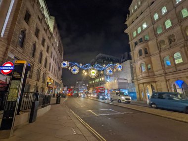Londra, İngiltere - 21 Aralık 2021: The Strand 'in üzerinde kırmızı bir otobüs ve trafik asılı duran şenlikli Noel ışıkları ikonik West End caddesi sahnesinde gece Charing Cross istasyonunun yanındaki
