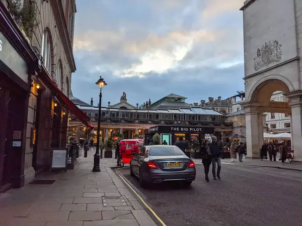 Londra, İngiltere - 05 Kasım 2021: İnsanlar Covent Garden 'ın ünlü pazar binasının yanında bulutlu bir gökyüzü altında dükkanları ve restoranlarıyla bir cadde boyunca yürüyor