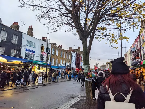 Londra, İngiltere - 27 Kasım 2021: Camden High Caddesi 'nin ıslak kaldırımlarında, bulutlu bir sonbahar gününde, seçkin dükkanları ve alternatif kültürüyle ünlü, canlı bir kalabalık yürüyor.