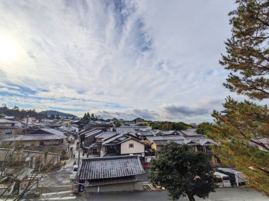 Kyoto, Japonya - 16 Aralık 2023: Geleneksel maçya evleri, kiremitli çatılar ve pitoresk bir gökyüzü altında uzak dağların yer aldığı tarihi Higashiyama bölgesinin manzarası yükseldi