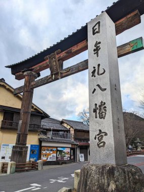 Shiga, Japonya - 20 Aralık 2023: Tarihi Himure Hachimangu Shinto tapınağının girişini belirleyen kanji yazısıyla geleneksel ahşap bir Torii kapısı ve taş sütun