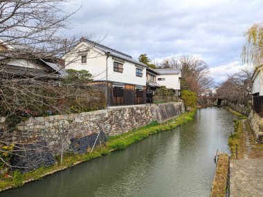 Shiga, Japonya - 20 Aralık 2023: Geleneksel beyaz duvarlı kura depoları ve tüccar evleri, güzel korunmuş bir su yolu olan tarihi Hachiman-bori Kanalı 'nın taş kıyıları hizasında.