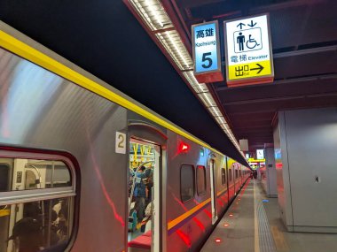 Kaohsiung, Tayvan - 02 Aralık 2022: İçinde yolcular bulunan modern bir banliyö treni, Kaohsiung tren istasyonunda iki dilde işaretli bir yeraltı platformunda duruyor.