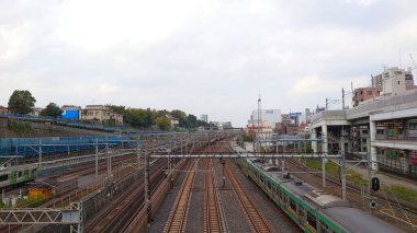 Tokyo, Japonya - 31 Ekim 2019: Nippori İstasyonu 'nda bulutlu bir gökyüzü altında kentsel binalarla çevrili karmaşık demiryolu rayları ve trenlerin geniş bir görünümü