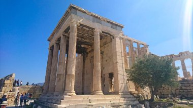 Atina, Yunanistan - 29,3,2018: Erekteyon 'un kuzey cephesindeki turistler, salgından önceki yaz güneşli açık mavi gökyüzü altında mermer sütunlarla desteklenen bir verandaya sahipler