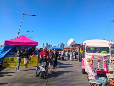 London, UK - April 05 2025: The lively outdoor Cutty Sark Street Food Market is bustling with diverse people browsing food stalls and enjoying a sunny day with the city skyline in the background