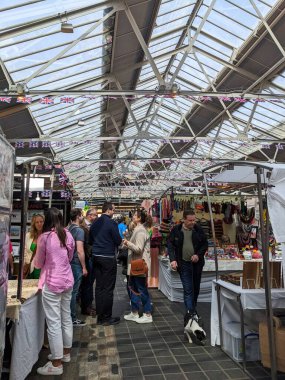 Londra, İngiltere - 2023.04.30: Ziyaretçiler, bulutlu bir günde Union Jack dekorasyon ve çatı pencereleri altında işlek Greenwich Pazarı 'nda el sanatları ve aksesuarları satan pazar tezgahlarına göz atıyorlar