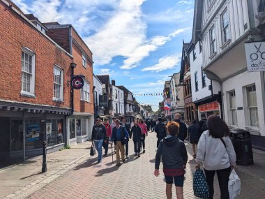 Canterbury, İngiltere - 19 Nisan 2025: Yayalar, tarihi Canterbury kentinde, bulutlu bir gökyüzü altında, St. Peters Caddesi 'ndeki geleneksel mağaza ve binaların önünden geçtiler
