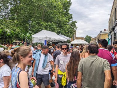 Londra, İngiltere - 2023.07.09: Müşteriler, bulutlu bir gökyüzünün altında Kolombiya Yolu Çiçek Pazarı 'ndaki pazar tezgahlarında bitki ve çiçeklere bakıyorlar