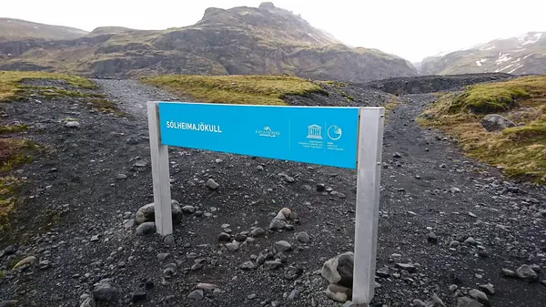 Solheimajokull, İzlanda - 3.26.2018: Solheimajokull Buzulu 'nun girişinde turistler olmadan sisli bir gökyüzünün altında kayalık dağlar, toprak yollar ve çimenler arasında bir işaret