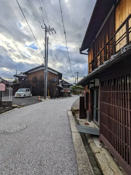 Omihachiman, Japonya - 12.20.2023: Trafiksiz geleneksel bir Japon caddesi tarihi ahşap binalarla kaplı bulutlu bir gökyüzü altında sakin bir kasaba manzarası