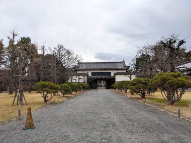 Kyoto, Japonya - 2023.12.16: Nijo Şatosu Kita Otemon Nijo Kalesi 'nde tuğla ve ahşap yapıya giden ağaçlı bir patika ile bulutlu bir gökyüzünün altında geleneksel çatı kiremitleri.