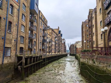Londra, İngiltere - 05.13.2024: St Saviours Rıhtımı 'nın tarihi rıhtımları ve ambarları Thames Nehri' nin açık çamurlu düzlüklerine tepeden bakıyor bulutlu bir gökyüzü altında