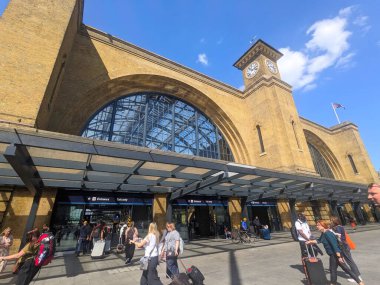 Londra, İngiltere - 03 Mayıs 2025: Bavullu insanlar güneşli bir günde açık mavi bir gökyüzü altında Kings Cross tren istasyonunun tarihi girişinden geçtiler