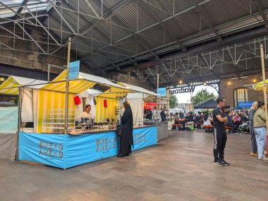 Londra, İngiltere - Mayıs 03 2025: İnsanlar popüler Ekmek Önündeki Fırın standında toplanıyor ve canlı tepe örtüsü pazarındaki ortak masalarda oturuyor, endüstriyel tarzda bir çatı altında canlı atmosferin tadını çıkarıyorlar.